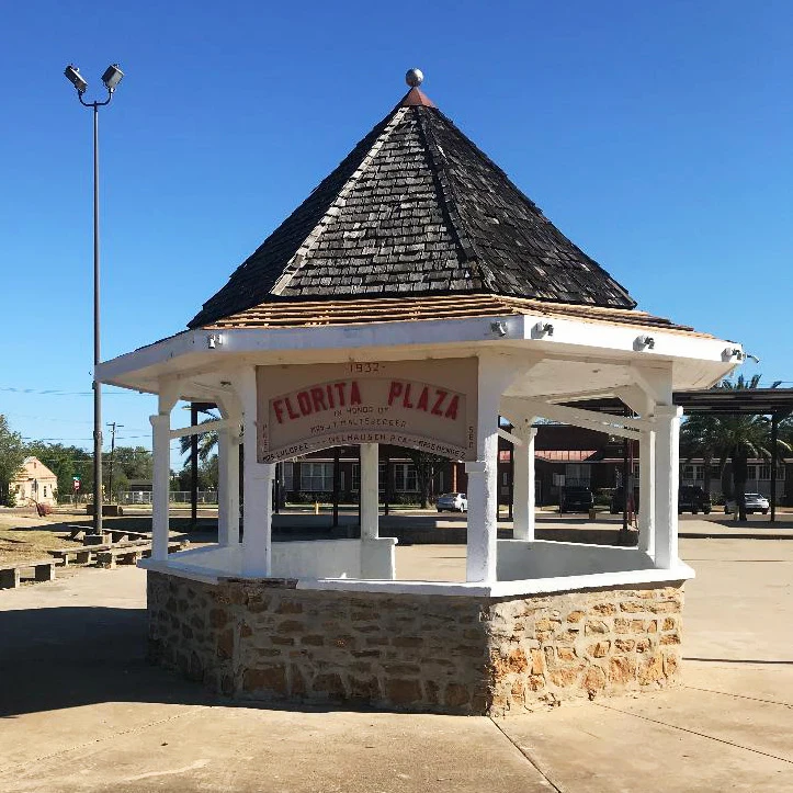 Historic Florita Plaza gazebo with its stone base, white columns, and dedication sign
